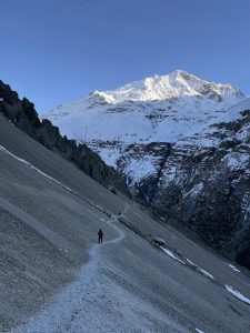A person hiking along a narrow path in a snowy mountain landscape, under a clear sky.