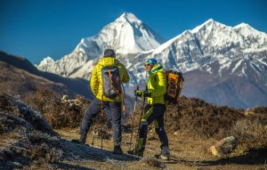 Two hikers enjoy a scenic trek in Mudi, with snowy peaks in the background.